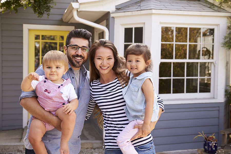 Personal Insurance - Portrait of a Smiling Family with Two Young Daughters Standing Outside Their New Home